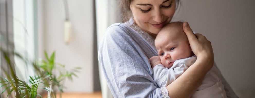 Smiling mid-adult mother holding her newborn baby in her home bedroom.