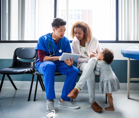 Male nurse talking and showing information on a digital tablet to a mother and her toddler in a hospital office