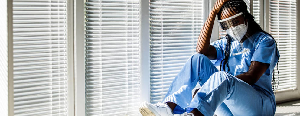 Overwhelmed nurse wearing PPE sitting down in a hospital hallway
